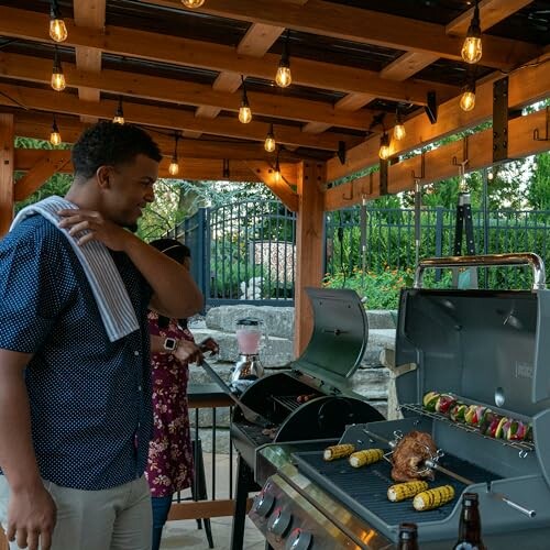 People grilling food on a barbecue under a pergola with string lights.