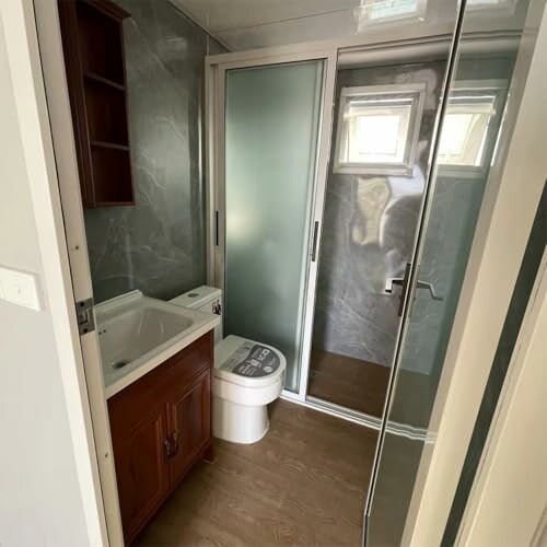 Compact bathroom with sink, toilet, and glass shower enclosure.