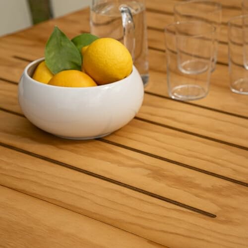 Bowl of lemons on wooden table with glasses and pitcher