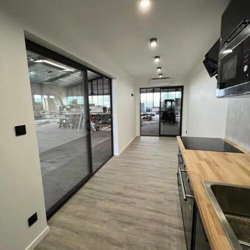 Modern kitchen space with industrial view, featuring large glass doors, wooden countertop, and appliances.