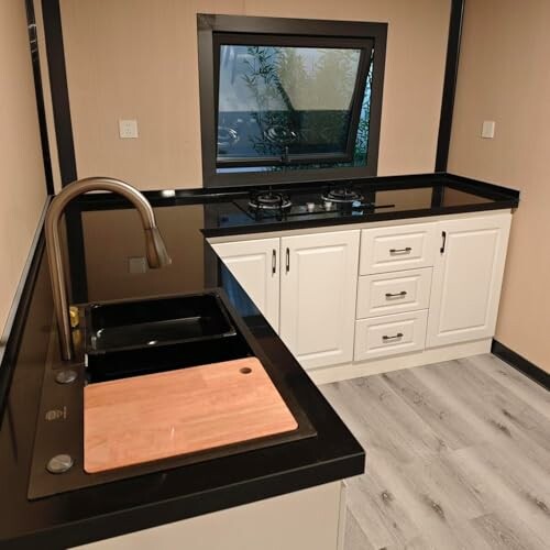 Modern kitchen with black countertops, sink, cutting board, stove, and window.