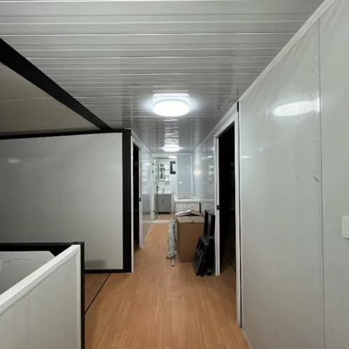 Interior view of a modern office corridor with wooden flooring and white walls.