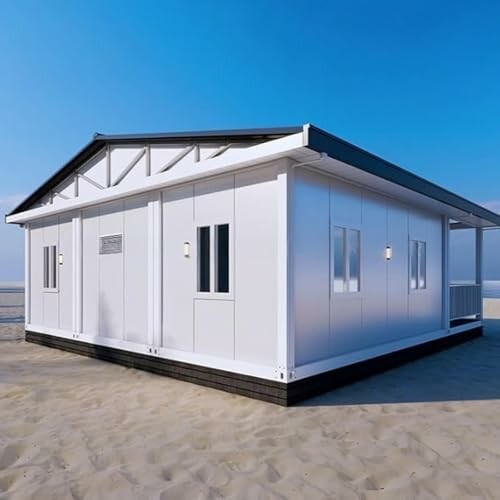 A modern modular house on a sandy beach under a clear blue sky.